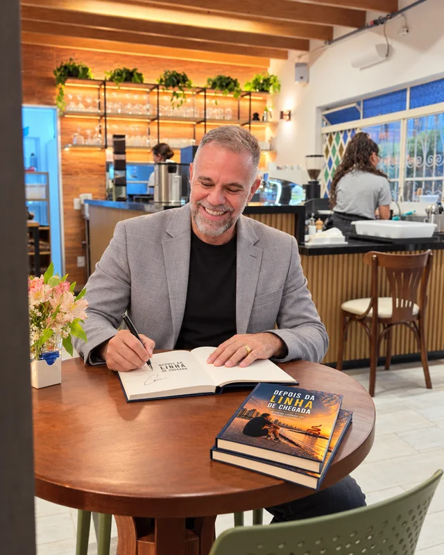 Composição ilustrativa de César Aarão autografando Depois da Linha de Chegada à mesa do O Jardim, com aliança na mão esquerda